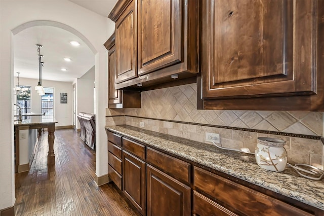 kitchen featuring arched walkways, dark wood finished floors, baseboards, decorative backsplash, and light stone countertops