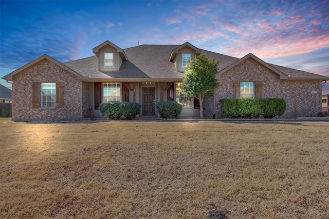 view of front facade featuring brick siding, a front yard, and a shingled roof