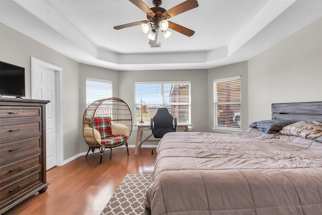 bedroom with a raised ceiling, ceiling fan, baseboards, and wood finished floors