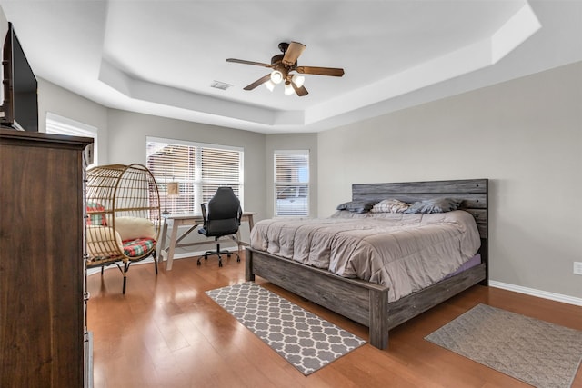 bedroom featuring a raised ceiling, visible vents, baseboards, and wood finished floors