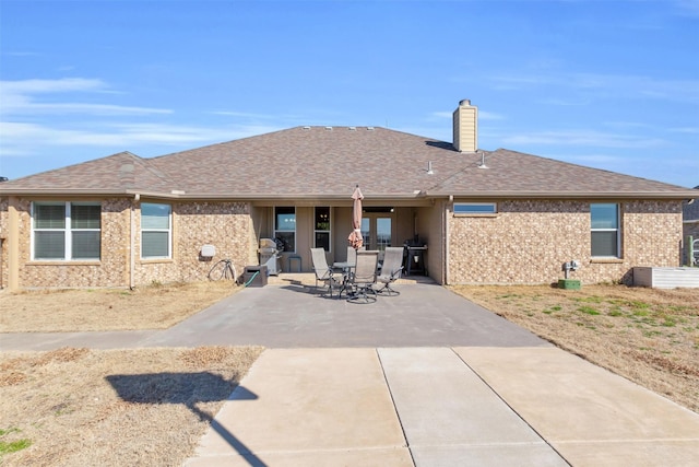 back of property with a chimney, brick siding, roof with shingles, and a patio area