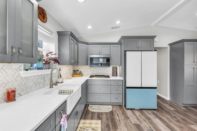 kitchen featuring lofted ceiling with beams, appliances with stainless steel finishes, wood finished floors, and gray cabinetry