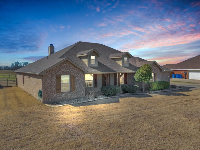 view of front of property with a shingled roof, brick siding, fence, a front lawn, and a chimney