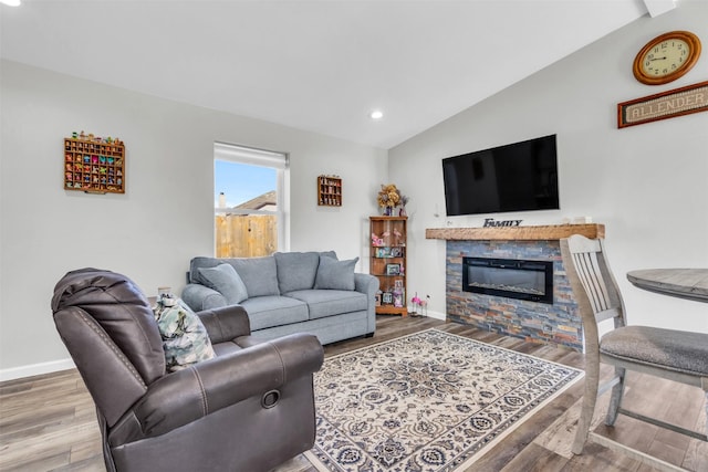 living area with lofted ceiling, a stone fireplace, wood finished floors, and baseboards