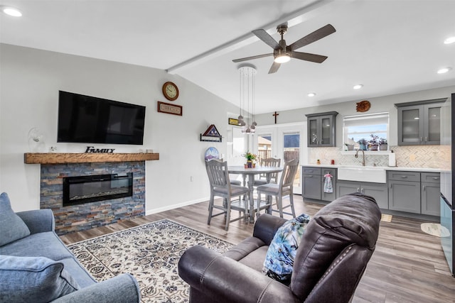 living area with baseboards, lofted ceiling with beams, light wood-style flooring, a fireplace, and recessed lighting