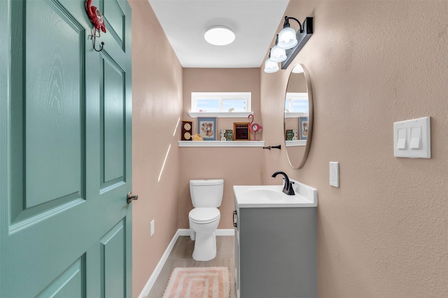 half bath with baseboards, vanity, and toilet