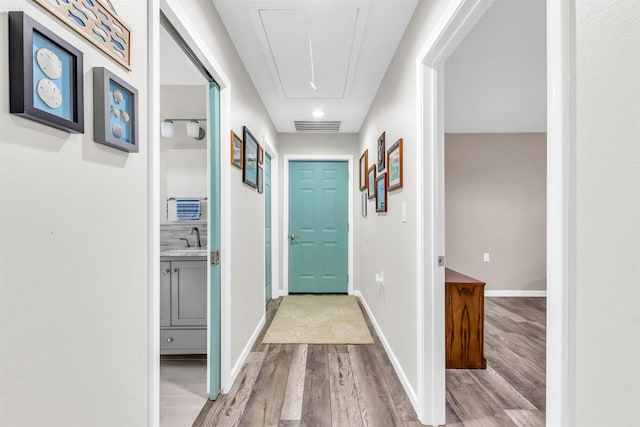 hall featuring attic access, baseboards, visible vents, wood finished floors, and a sink