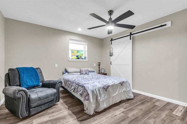 bedroom featuring recessed lighting, a barn door, ceiling fan, wood finished floors, and baseboards