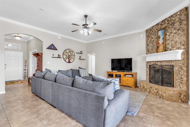 living room featuring arched walkways, ceiling fan, crown molding, a fireplace, and light tile patterned flooring