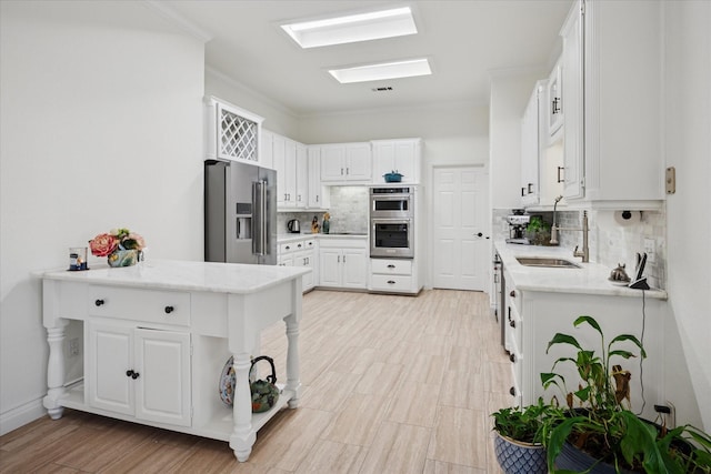 kitchen featuring appliances with stainless steel finishes, a skylight, a sink, and white cabinets