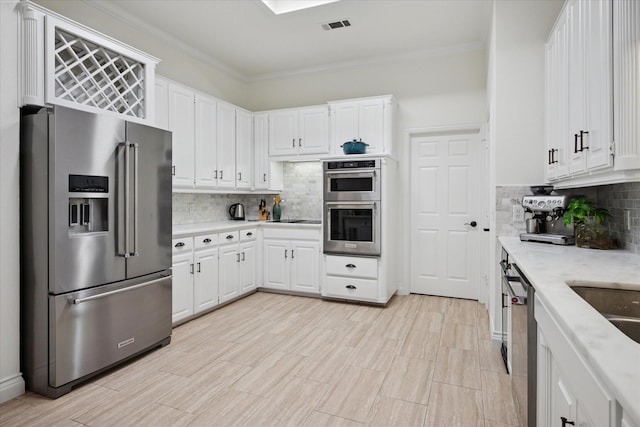 kitchen featuring appliances with stainless steel finishes, white cabinetry, ornamental molding, and decorative backsplash