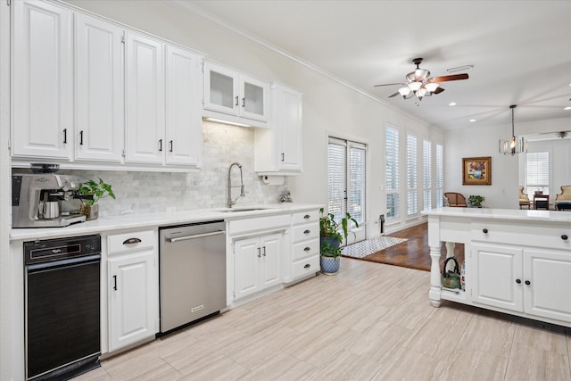 kitchen featuring tasteful backsplash, white cabinets, dishwasher, light countertops, and a sink