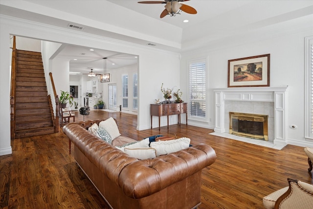 living area featuring visible vents, a tile fireplace, ceiling fan, wood finished floors, and stairs