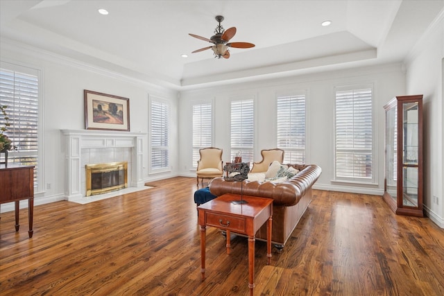 living room featuring baseboards, a tray ceiling, wood finished floors, and a tile fireplace