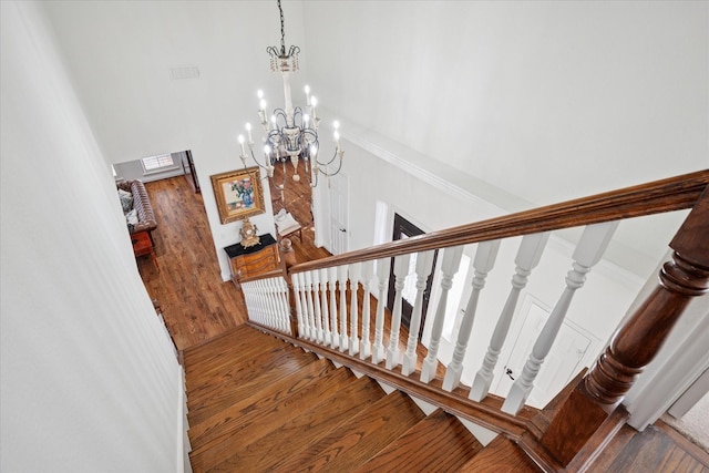 stairway featuring visible vents, a notable chandelier, a towering ceiling, and wood finished floors