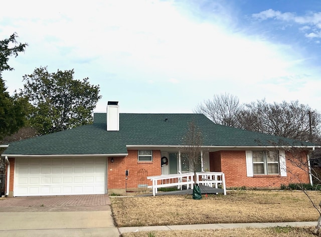 ranch-style home with a porch, an attached garage, brick siding, decorative driveway, and a chimney