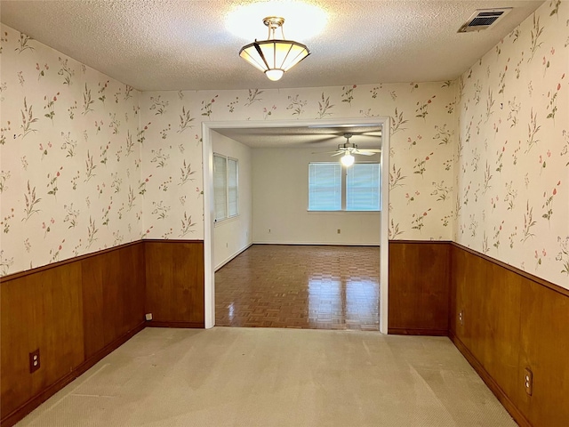 spare room featuring wallpapered walls, a textured ceiling, visible vents, and a wainscoted wall