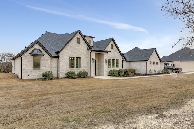 french provincial home with brick siding, a front lawn, and roof with shingles