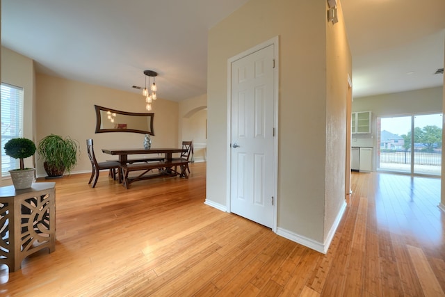 dining space with arched walkways, light wood-type flooring, and baseboards