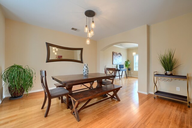 dining area featuring light wood-style floors, arched walkways, visible vents, and baseboards