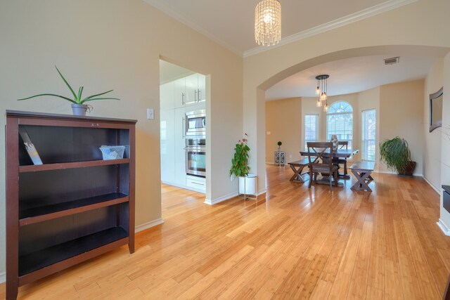 dining space featuring arched walkways, an inviting chandelier, light wood-style floors, ornamental molding, and baseboards