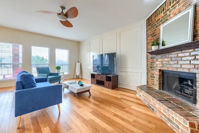 living area featuring light wood-style floors, a fireplace, a decorative wall, and a ceiling fan