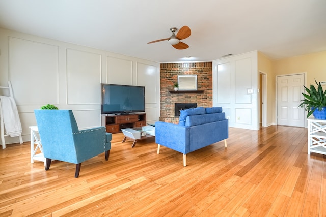 living room featuring a fireplace, visible vents, a decorative wall, light wood-style floors, and a ceiling fan