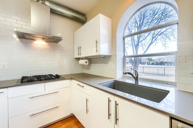 kitchen featuring stainless steel gas cooktop, wood finished floors, a sink, white cabinets, and wall chimney range hood