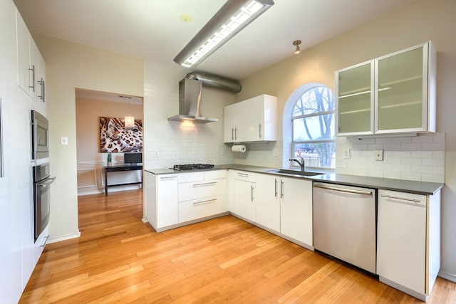 kitchen with stainless steel appliances, light wood-type flooring, a sink, and wall chimney range hood