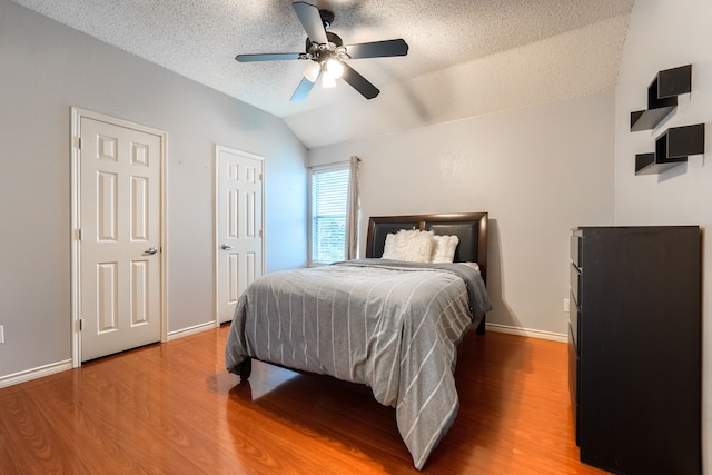 bedroom featuring vaulted ceiling, a textured ceiling, baseboards, and wood finished floors