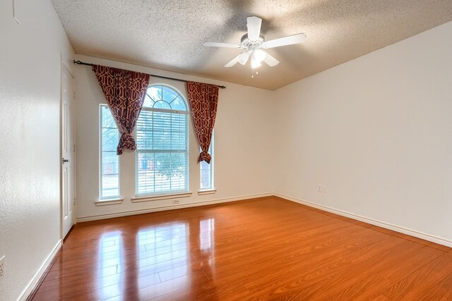 empty room featuring a textured ceiling, ceiling fan, wood finished floors, and baseboards