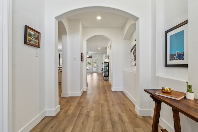 hallway featuring arched walkways, recessed lighting, baseboards, and light wood-style floors