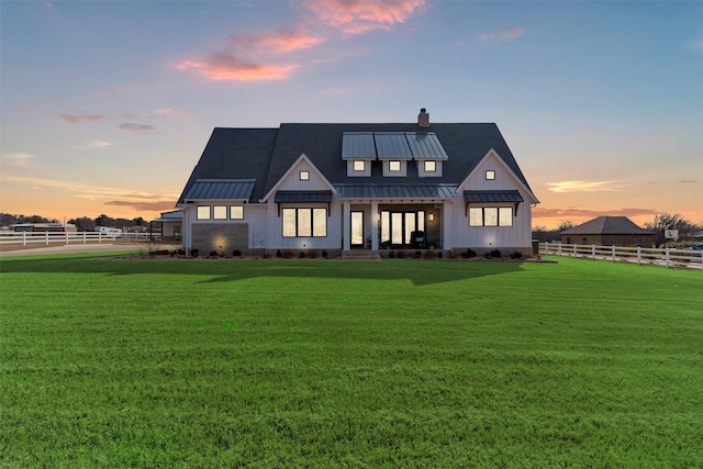 back of house at dusk with a standing seam roof, a lawn, metal roof, and fence