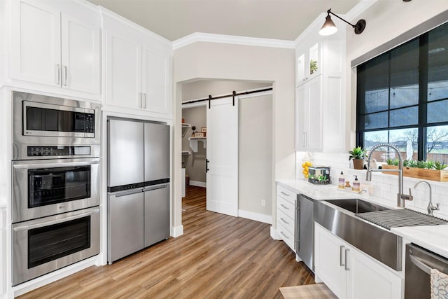 kitchen with a barn door, decorative backsplash, appliances with stainless steel finishes, crown molding, and a sink