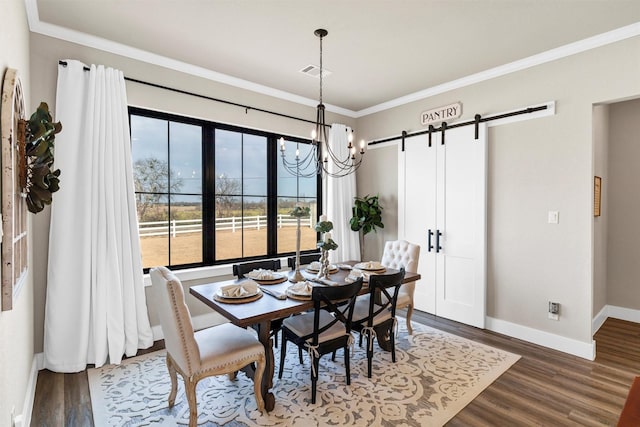 dining room with a barn door, baseboards, visible vents, wood finished floors, and crown molding