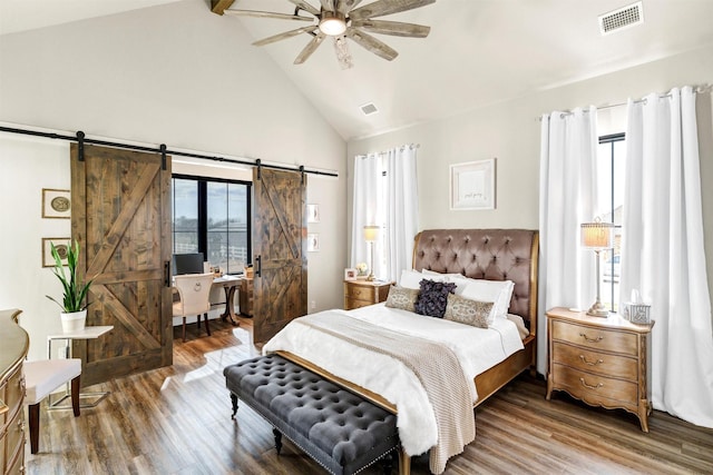 bedroom with high vaulted ceiling, wood finished floors, visible vents, and a barn door