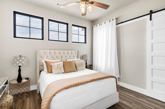 bedroom with dark wood-type flooring, visible vents, baseboards, and a barn door