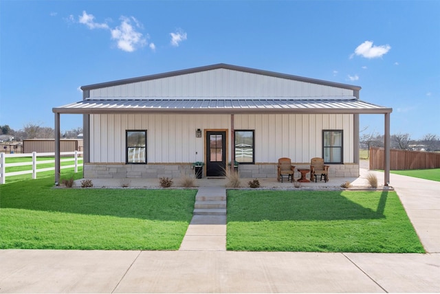 modern farmhouse style home with a front yard, stone siding, metal roof, and fence