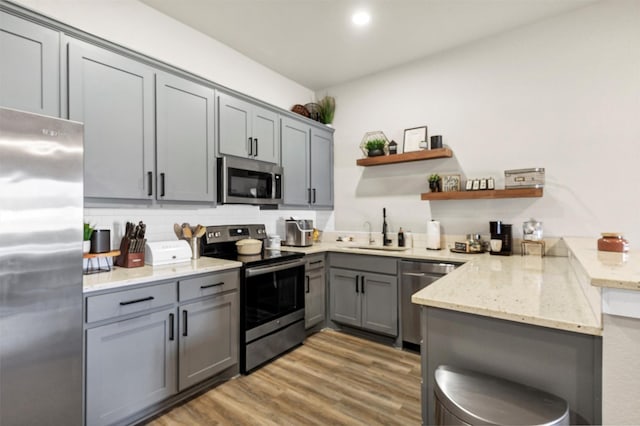 kitchen featuring light wood-style flooring, stainless steel appliances, a peninsula, a sink, and gray cabinets