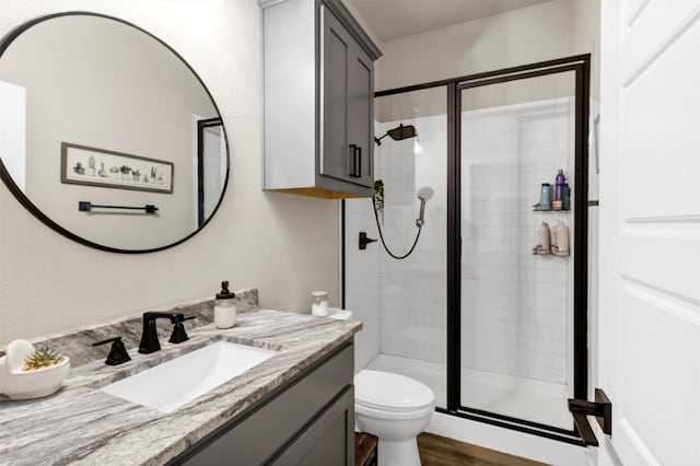 bathroom featuring wood finished floors, a shower stall, toilet, and vanity