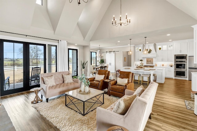 living area with a chandelier, high vaulted ceiling, light wood finished floors, and plenty of natural light