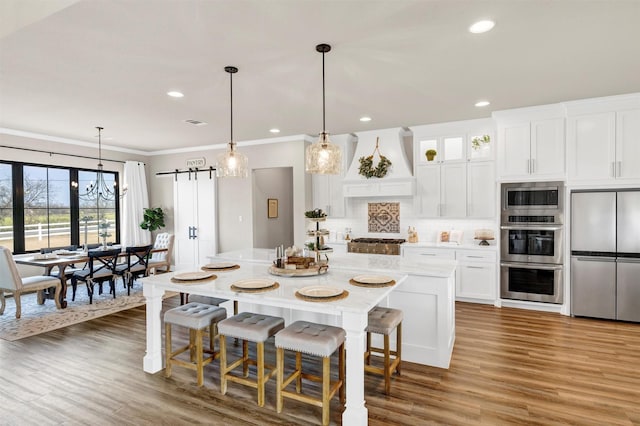 kitchen featuring stainless steel appliances, light countertops, custom range hood, backsplash, and a barn door