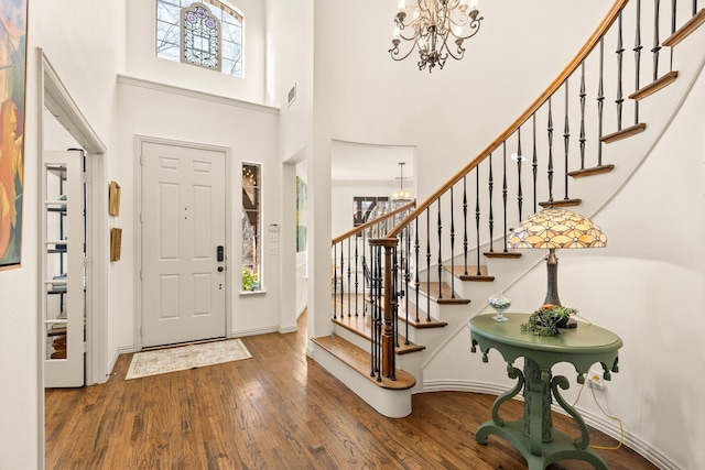 foyer entrance with a notable chandelier, visible vents, a towering ceiling, wood finished floors, and stairs