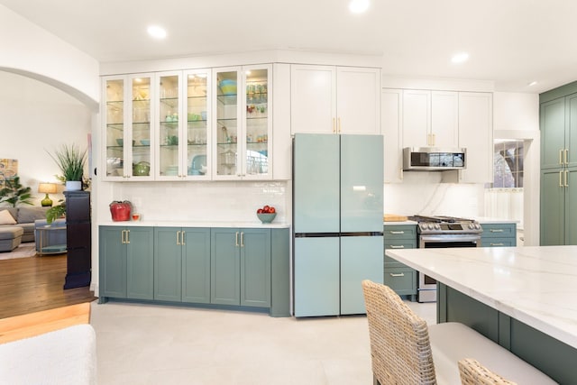 kitchen with decorative backsplash, glass insert cabinets, appliances with stainless steel finishes, light stone countertops, and white cabinetry