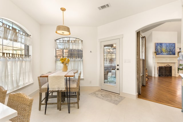 dining area featuring a healthy amount of sunlight, a fireplace, visible vents, and arched walkways