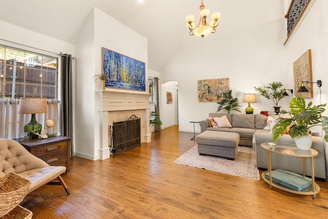 living room featuring arched walkways, high vaulted ceiling, a fireplace, wood finished floors, and an inviting chandelier