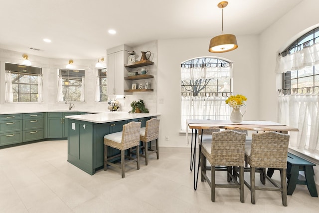 kitchen featuring a breakfast bar area, visible vents, light countertops, open shelves, and green cabinetry