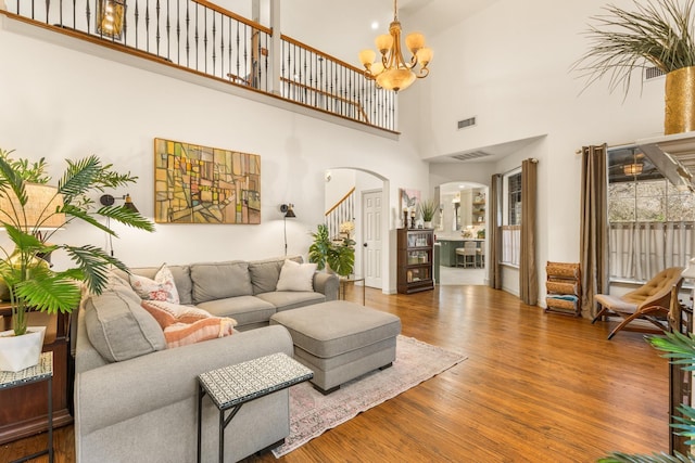 living room featuring visible vents, arched walkways, wood finished floors, stairs, and a chandelier