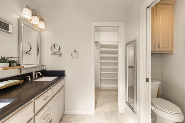 bathroom with a walk in closet, vanity, toilet, and baseboards