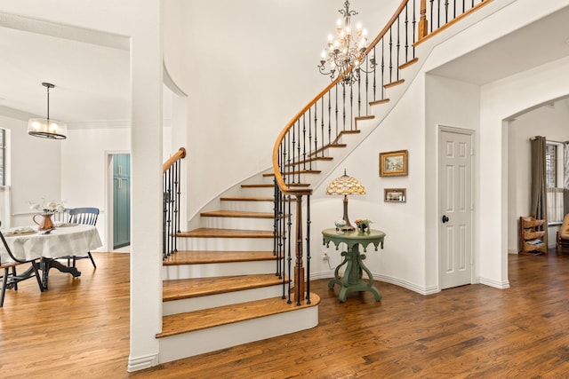 stairs with baseboards, arched walkways, a towering ceiling, wood finished floors, and a notable chandelier